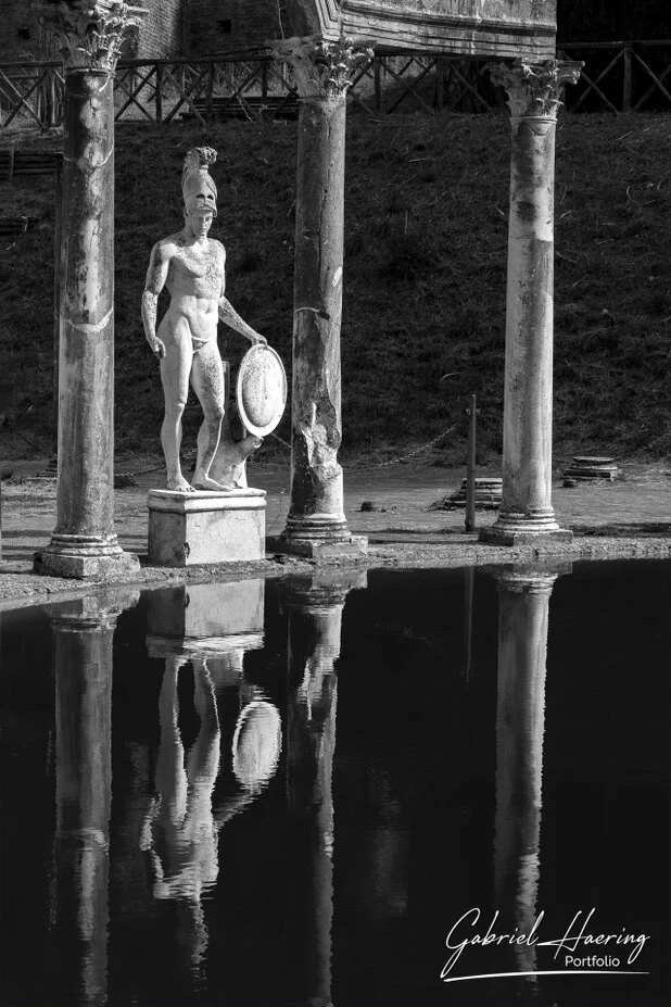 Black and white Roman warrior statue reflected between ancient columns